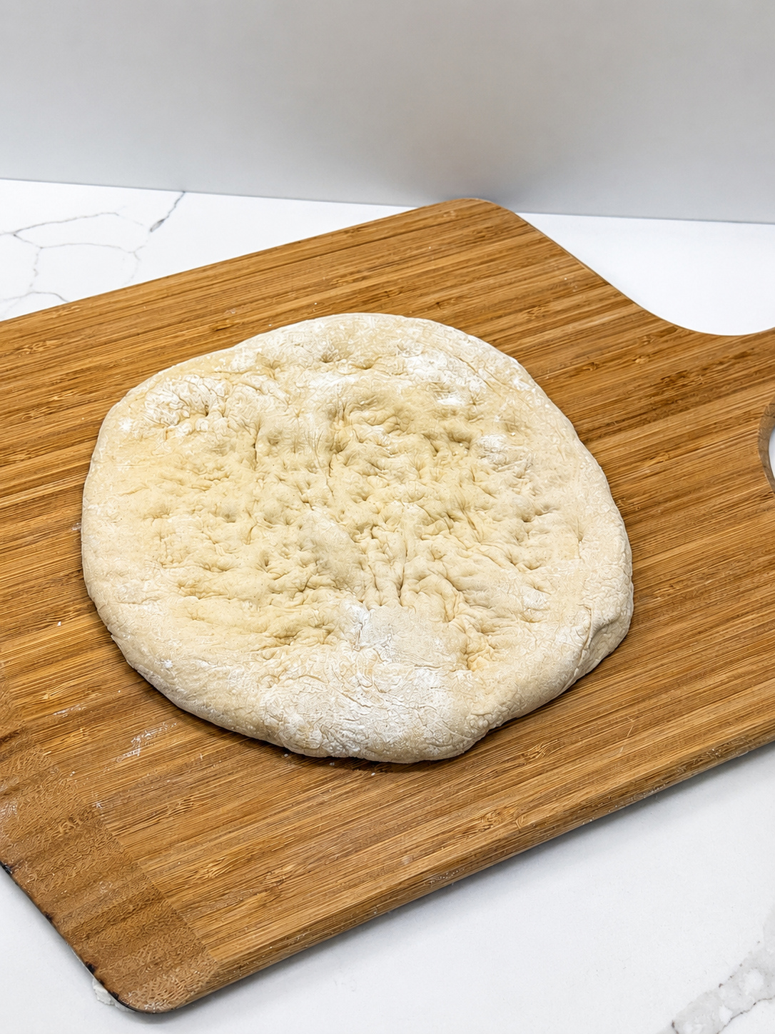 A hand-dimpled pizza dough disc on a wooden board